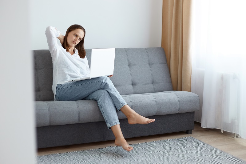 Młoda kobieta siedząca na sofie, z laptopem na kolanach